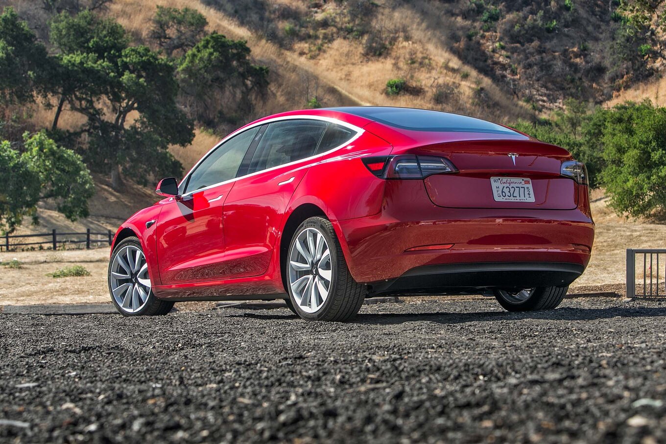 Red Model 3 driving down a lakeside road